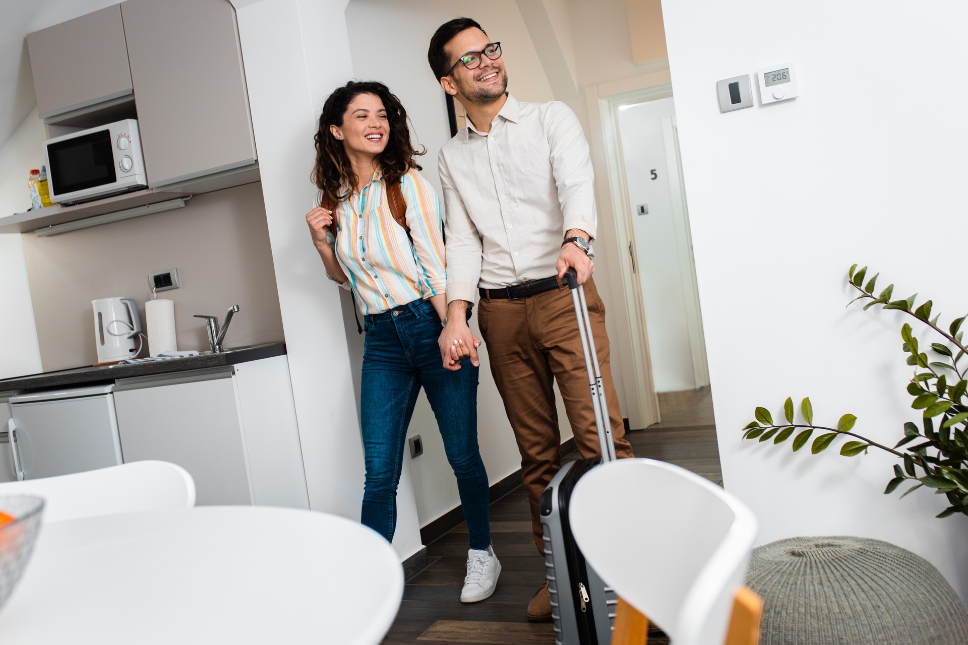 Smiling couple with suitcase arriving in apartment.